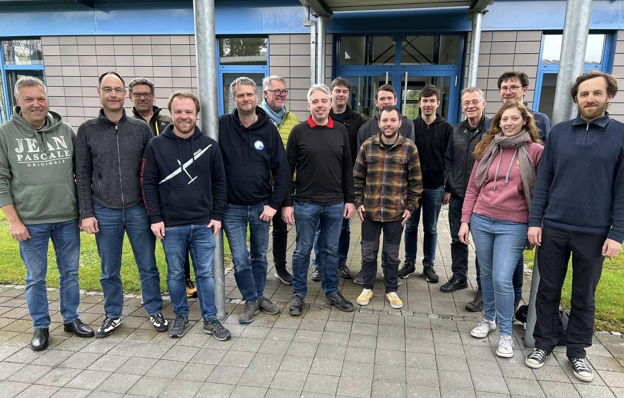 IMG_7730 Teilnehmer des Aeroclub NRW stehen in einem Halbkreis, nebeneinander vo einem Blau, grauen Gebäude. Im Hintergrund sieht man die Eingangstür.