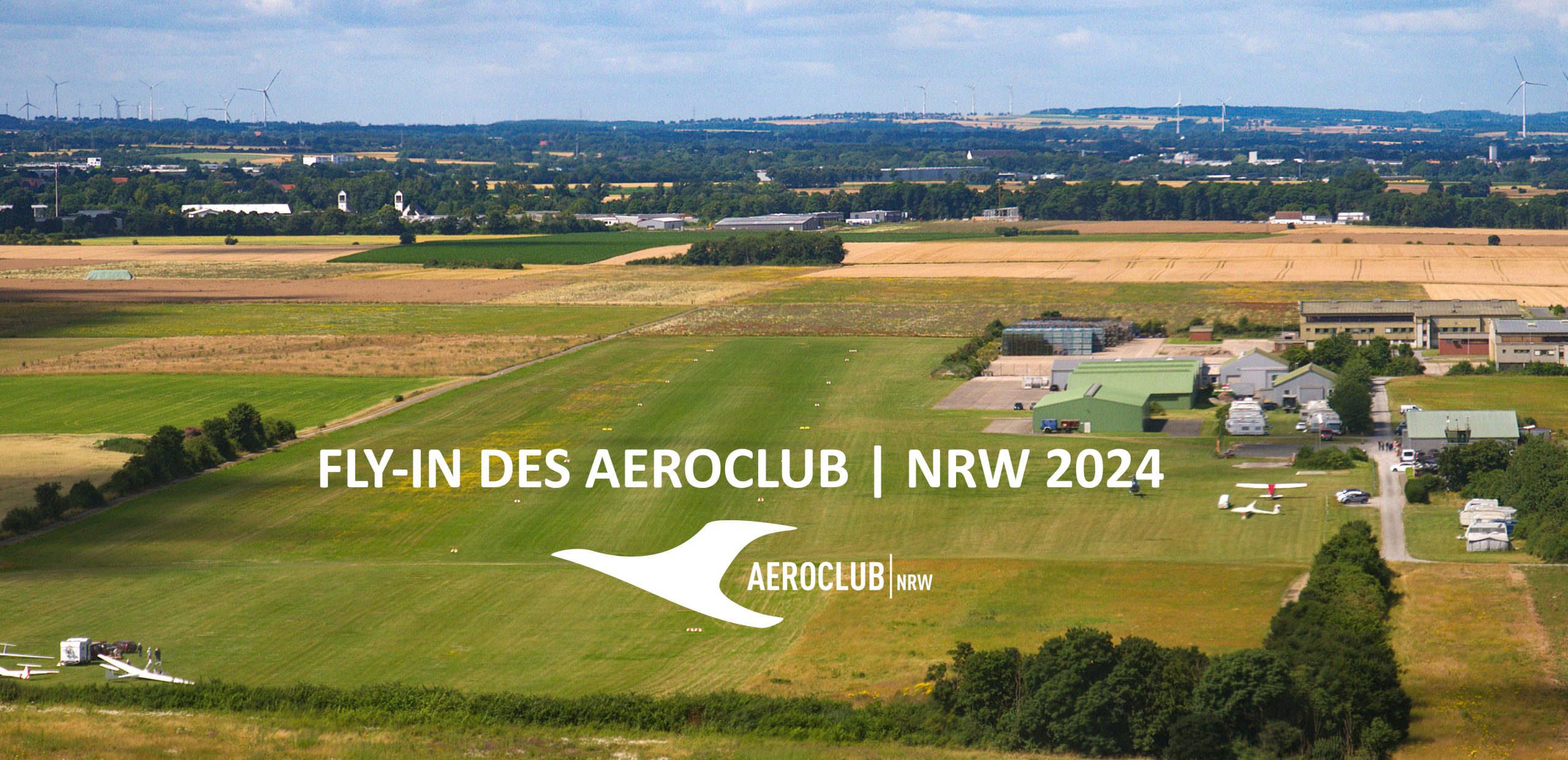 Fly-In 2024 Soest Fly-In 2024 Soest. Man sieht einen Flugplatz mit einer großen grünen Rasenfläche. Im Hintergrund sieht man ein paar Bäume, Felder und Häuser.