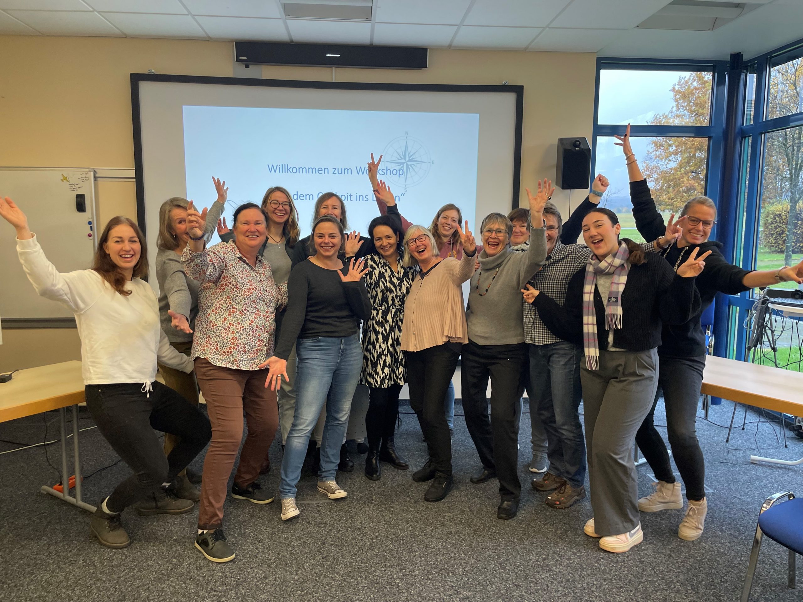 Sowohl Segelfliegerinnen als auch Motorfliegerinnen waren unter den 12 Teilnehmerinnen des Workshops von Anne Hennig. Sie stellten sich als Gruppe zusammen, vor die Leinwand auf der die Präsentation stattfand und machten ein Gruppenfoto. Alle halten die Arme in die Luft und Winken oder zeigen ein Peace Zeichen hoch.