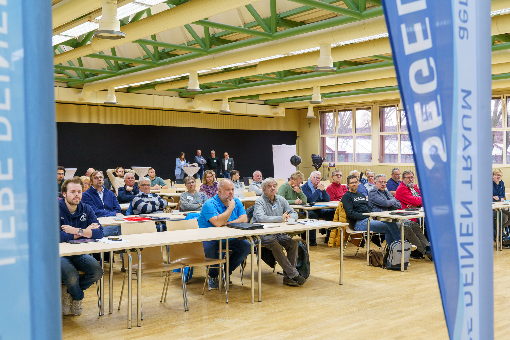 Jahreshauptversammlung Segelflug 2024 Jahreshauptversammlung Segelflug 2024 An mehreren Tischreihen in einer Aula, sitzen Mitglieder des Aeroclub|NRW. Hinter ihnen befinden sich Stehtische, die in weiße Tücher gehüllt sind.