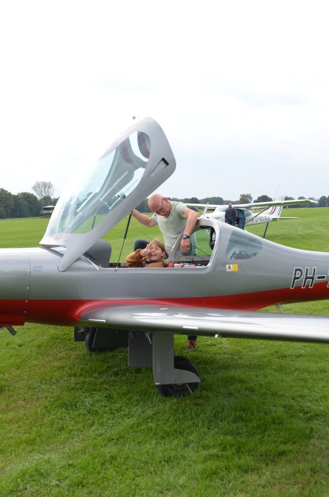 Mädchen zeigt lachend den Daumen hoch im Cockpit des Ultraleichtflugzeugs