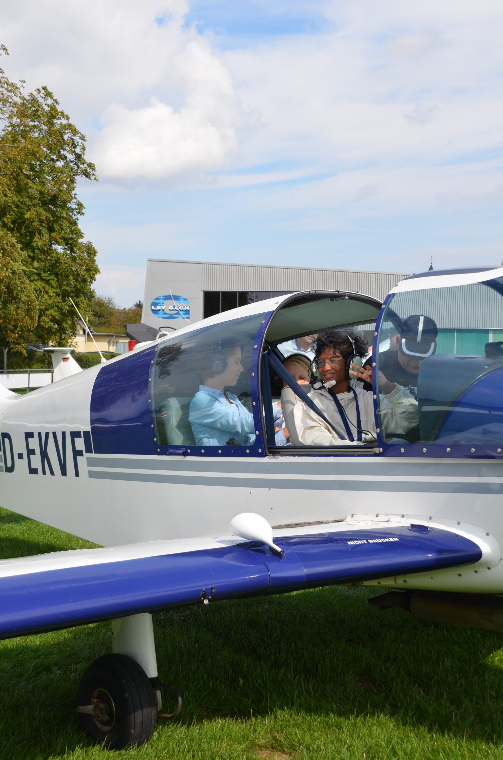 Mädchen mit Headset zeigt lachend das Peace-Zeichen im Cockpit des Motorflugzeugs D-EKVF