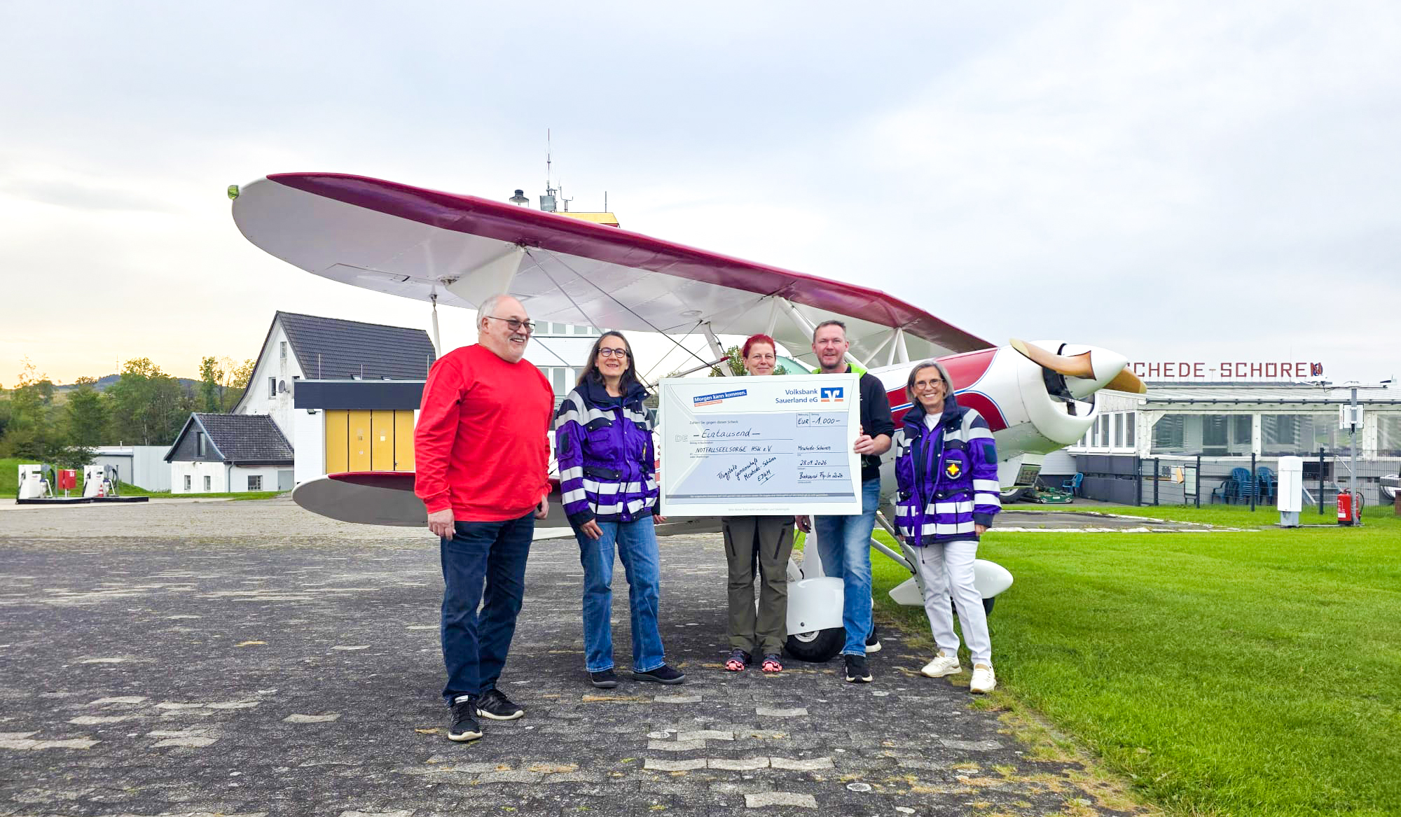 Scheckübergabe über 1.000 Euro vor einem Doppeldecker am Flugplatz Meschede-Schüren