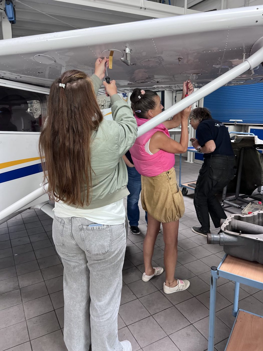 Pilotinnen schauen durch geöffnete Inspektionsdeckel unter der Tragfläche einer Cessna